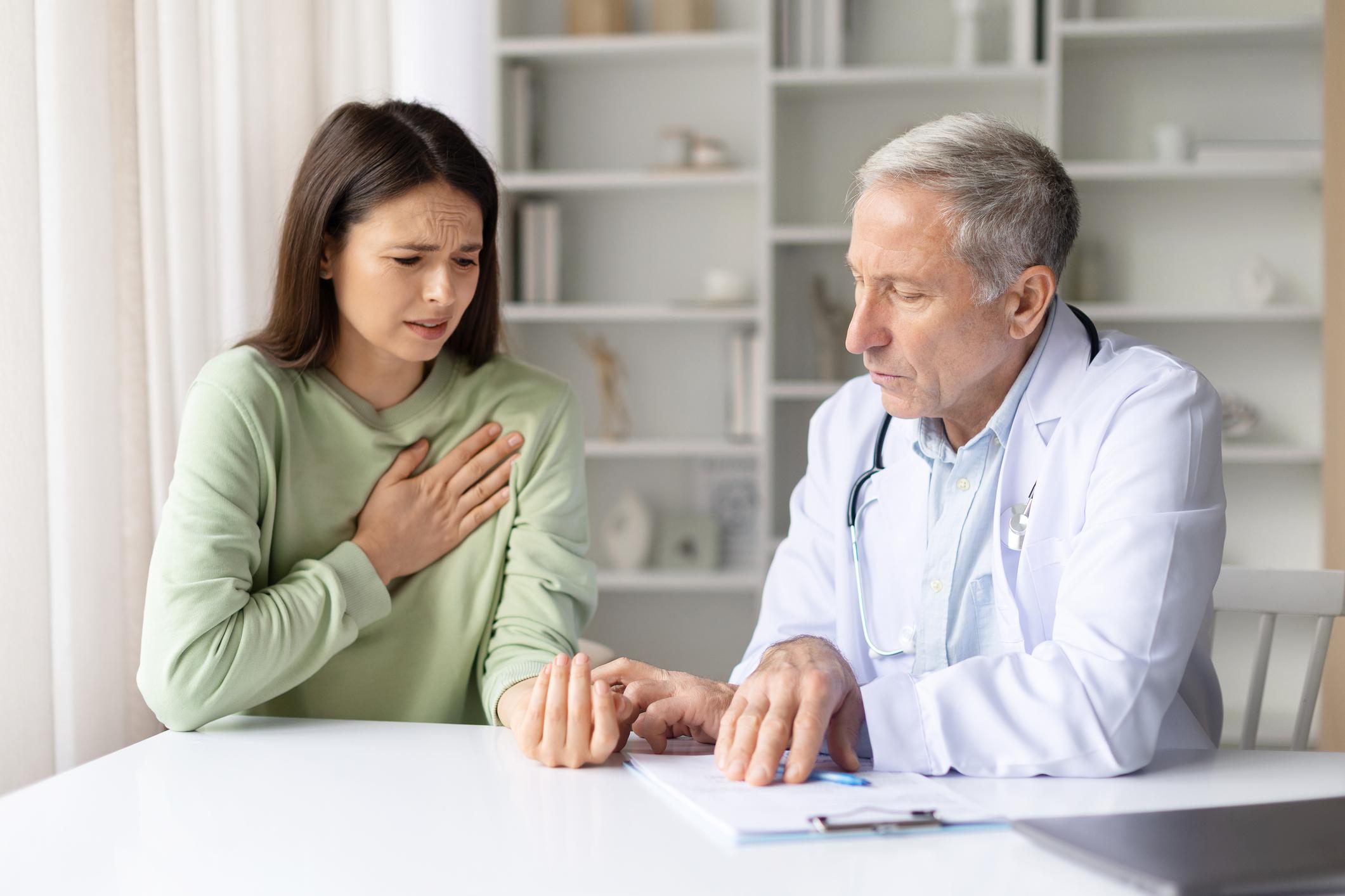 Female patient experiencing chest pain while doctor reviews medical information